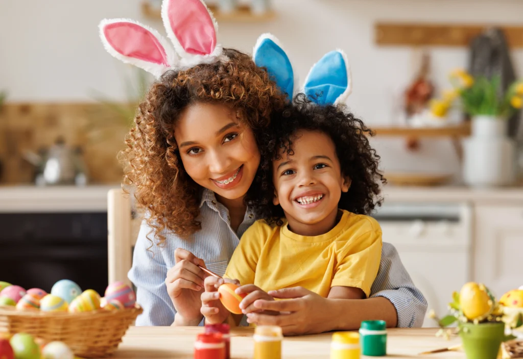 Smiling mother and child wearing bunny ears decorate an Easter egg together