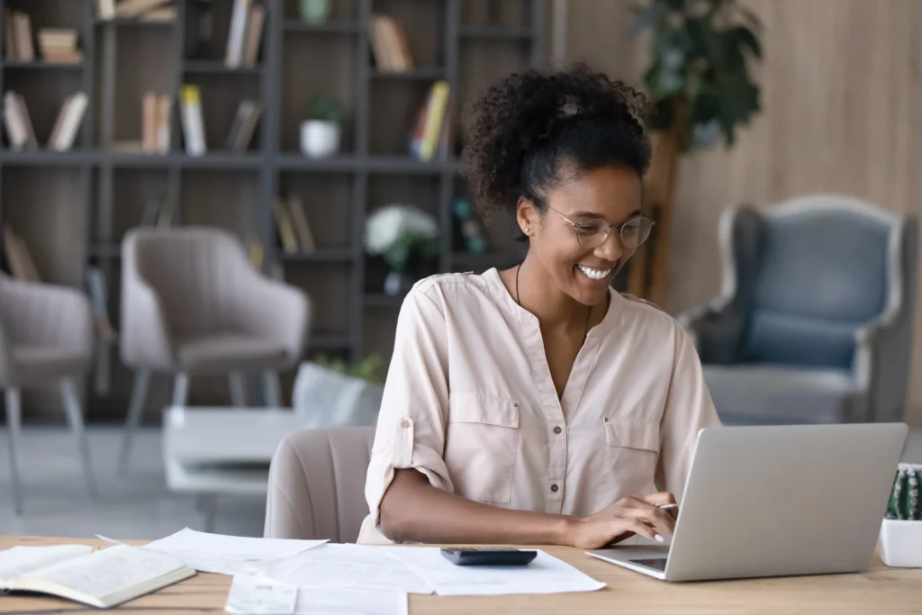 Smiling woman works on her laptop figuring out how to save money long term