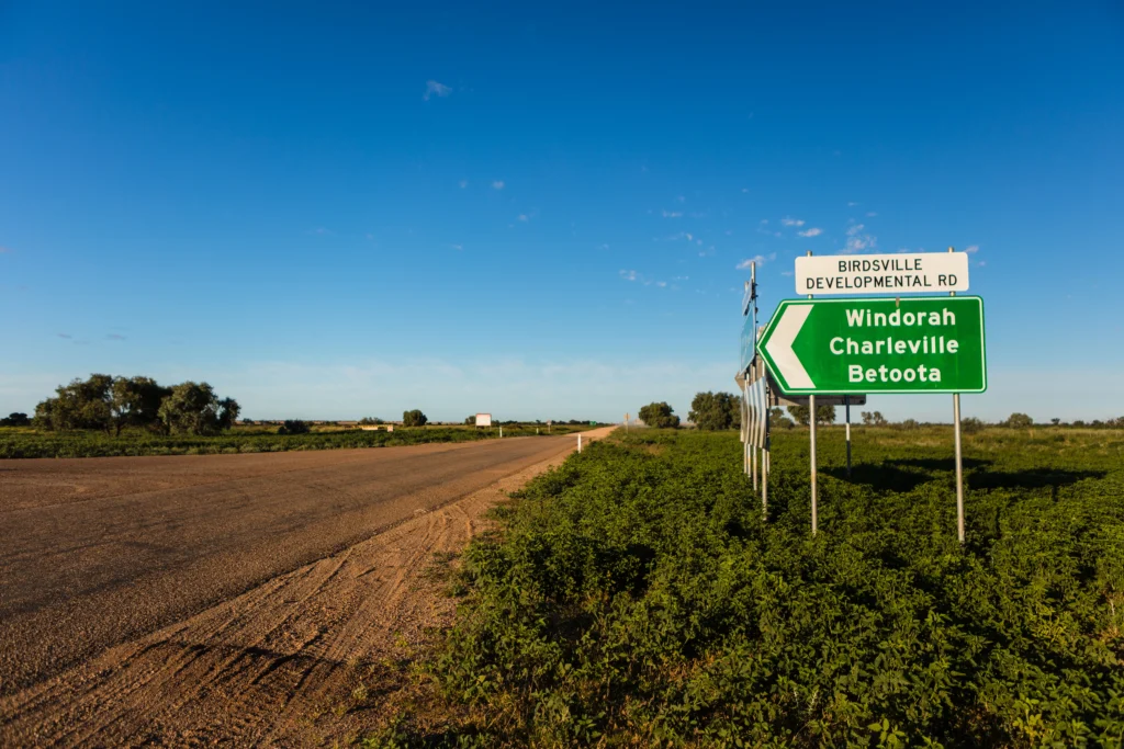 A dirt road in the outback with a road sign pointing to Windorah, Charleville, and Betoota