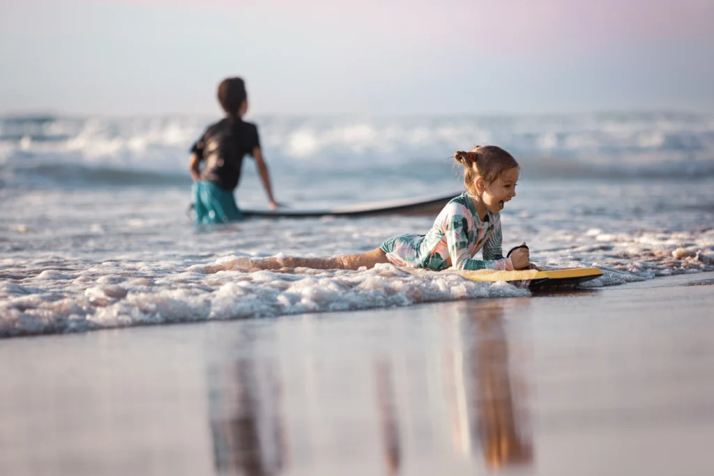 Two kids ride boogie boards on shallow waves at the beach