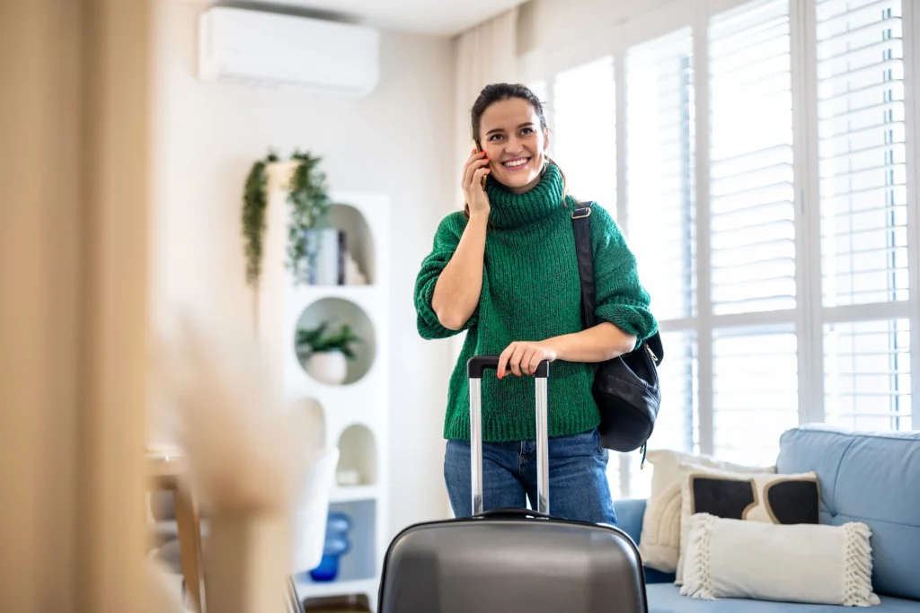 A woman in a green turtle neck holds the handle of a suitcase