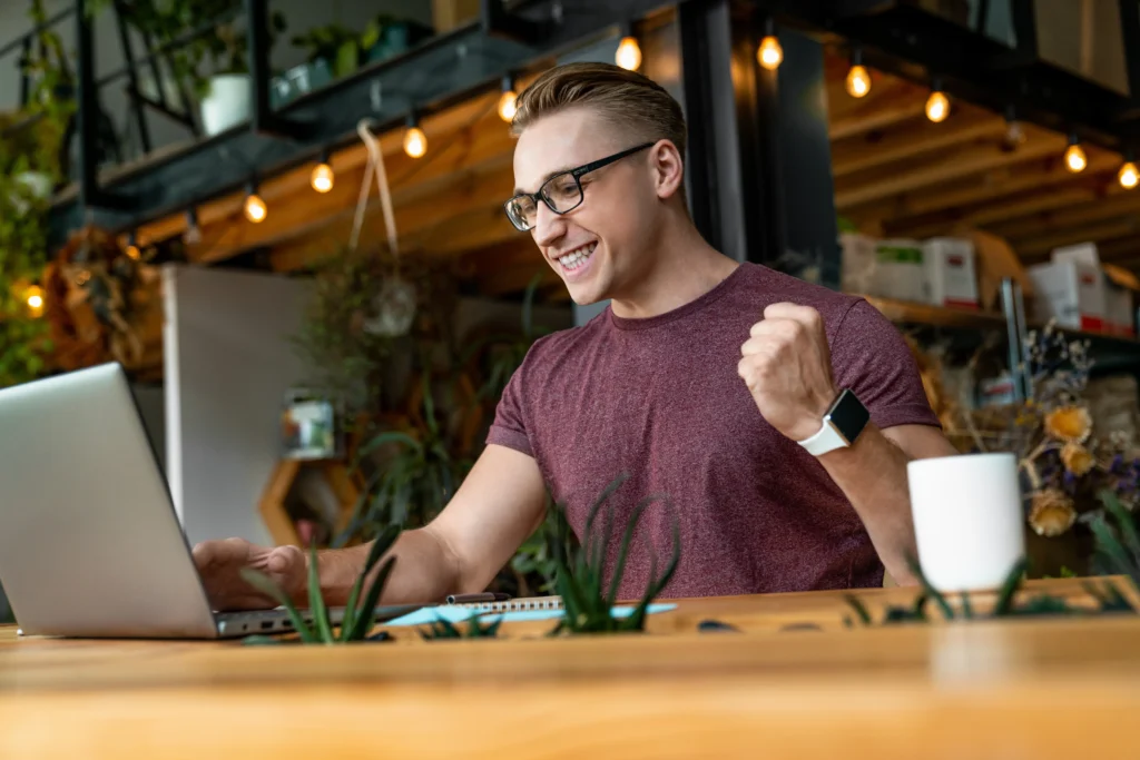 Man on his laptop in a cafe pumps his fist after getting an urgent loan with no credit check