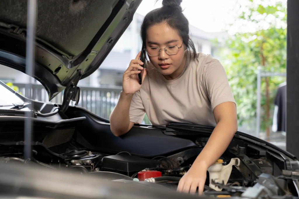 A woman looks under the bonnet of her car while calling a mechanic