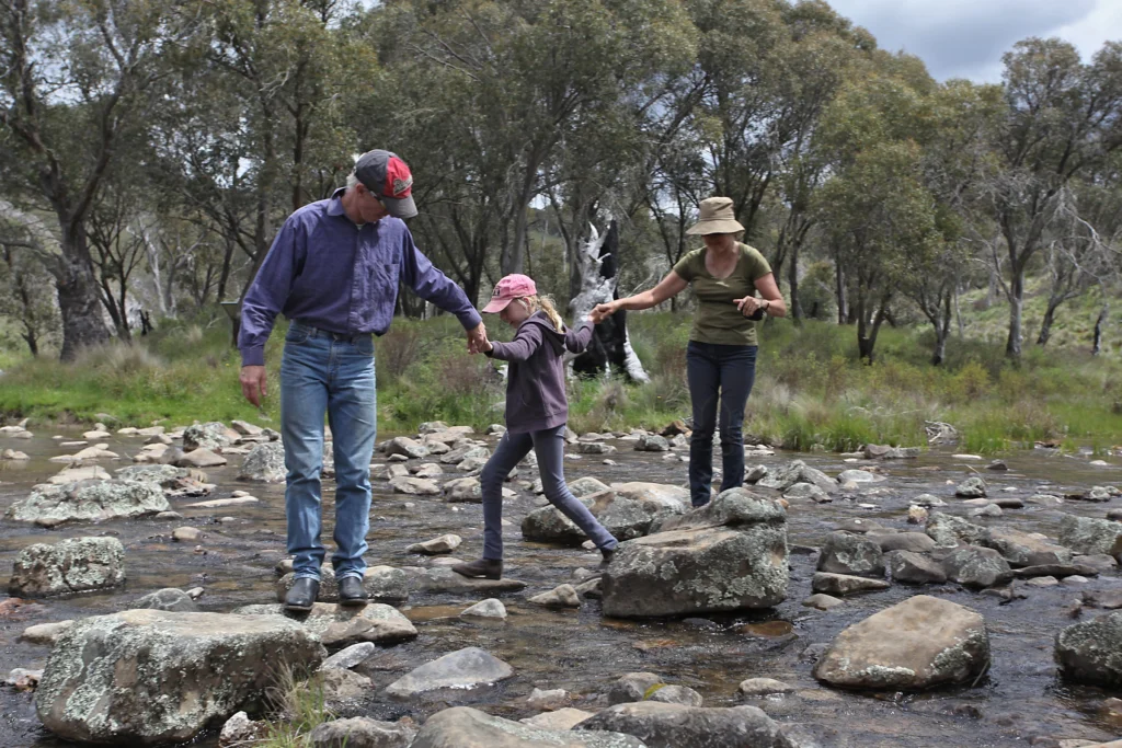 Grandma and grandpa on a hike, hopping rocks over a creek with their granddaughter