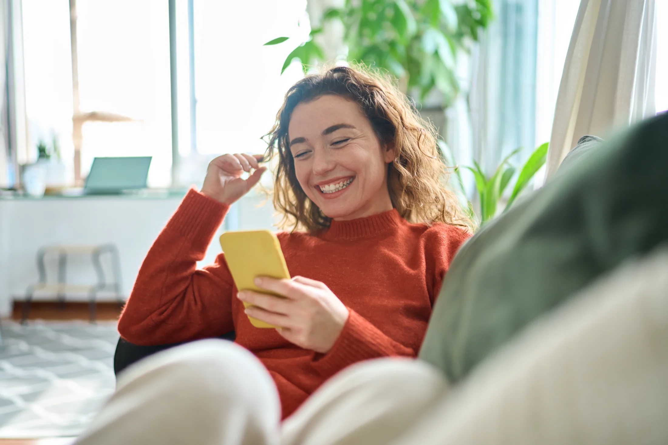 loans against cars; happy woman sitting on couch and using her phone | Swoosh Finance