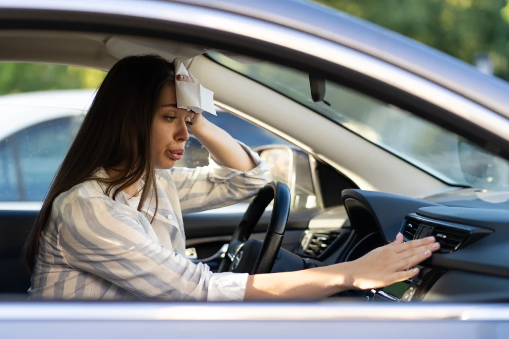 Woman driving car and sweating, dabbing cloth to her forehead and checking the AC