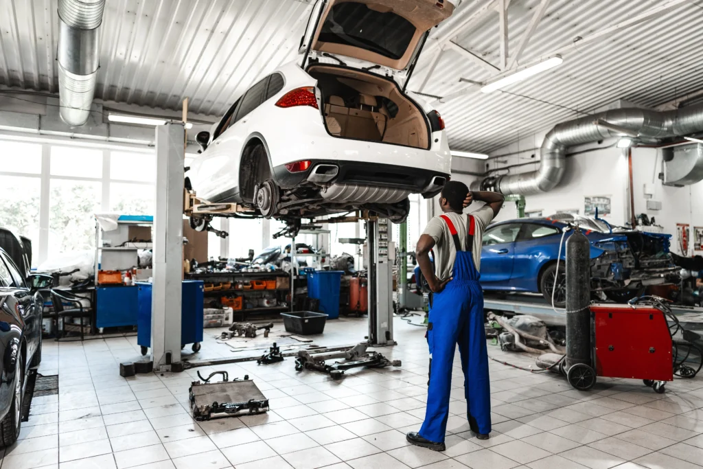 A mechanic shop with a raised car and man in overalls looking under it